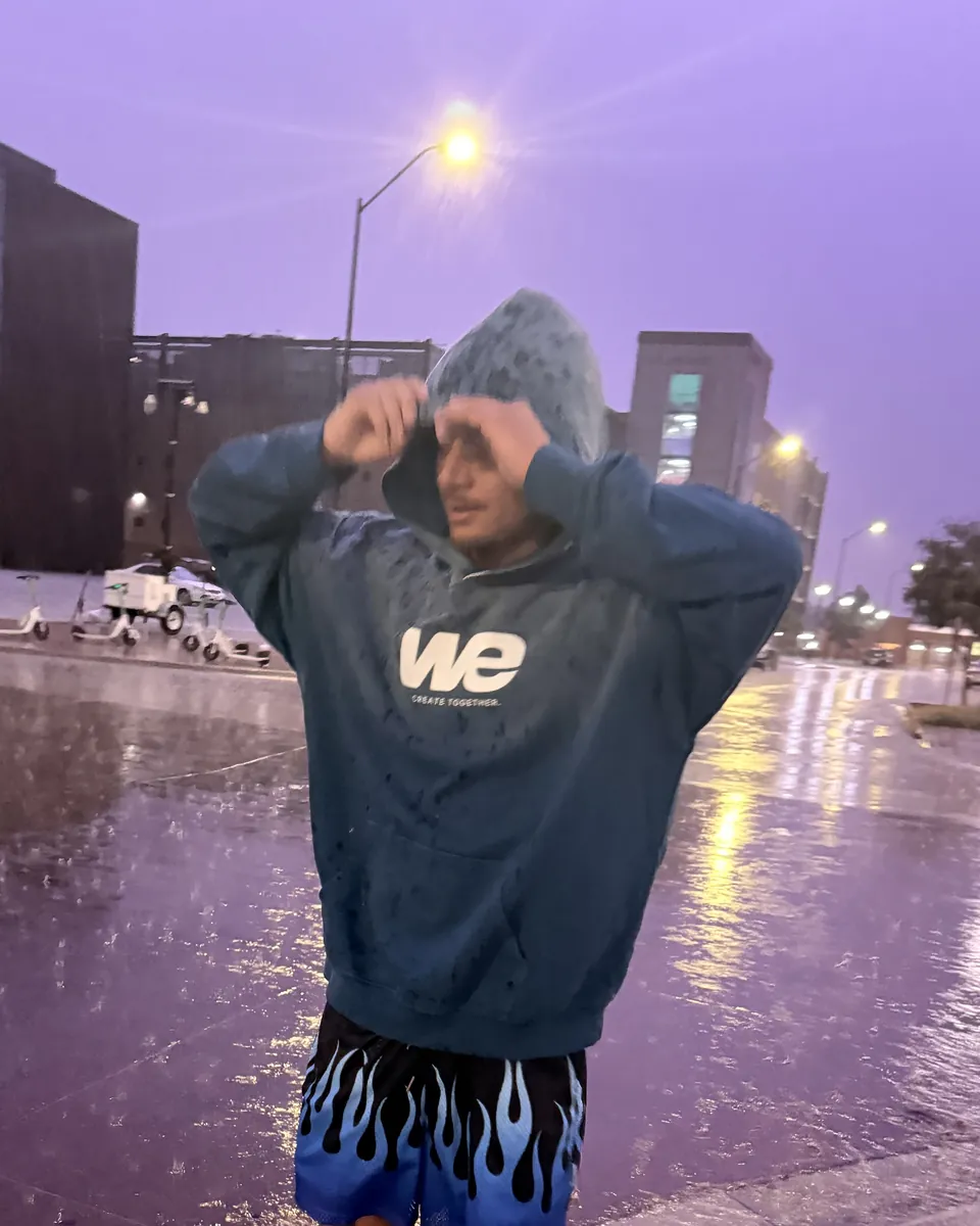 Pulling up the hood of a WE Hoodie in the rain on a wet street at dusk