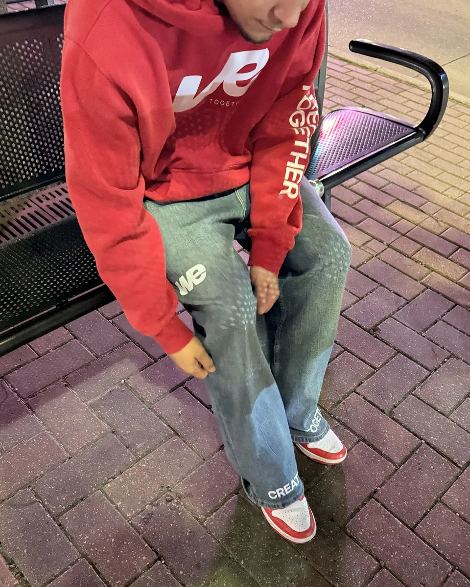 Sitting on a bench in the WE Gameday Hoodie and WE Sun Fade Denim, Create Together on the sleeve and the hem